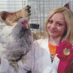 A young girl holds up a ribbon she won showing off her chicken