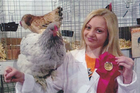 A young girl holds up a ribbon she won showing off her chicken