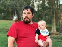 Man holding baby with chicken on shoulder
