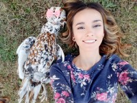 Lady posing with chicken laying on the ground