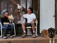 Couple on deck holding chickens with dog laying down